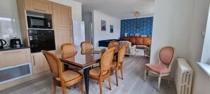 Una cocina compacta con electrodomésticos modernos, un comedor con sillas de mimbre y una pared con estampado azul.