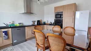 A modern kitchen with wooden cabinets, a glass-top dining table, and wicker chairs. - Beautiful renovated house in Lambell - 5min from beaches and Tregunc center (Trégunc)