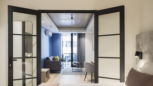 A modern hotel room with a bed, a desk, a chair, and a sofa. There is a view of the city through large windows. - Home Suite Hotels Station House (Cape Town)