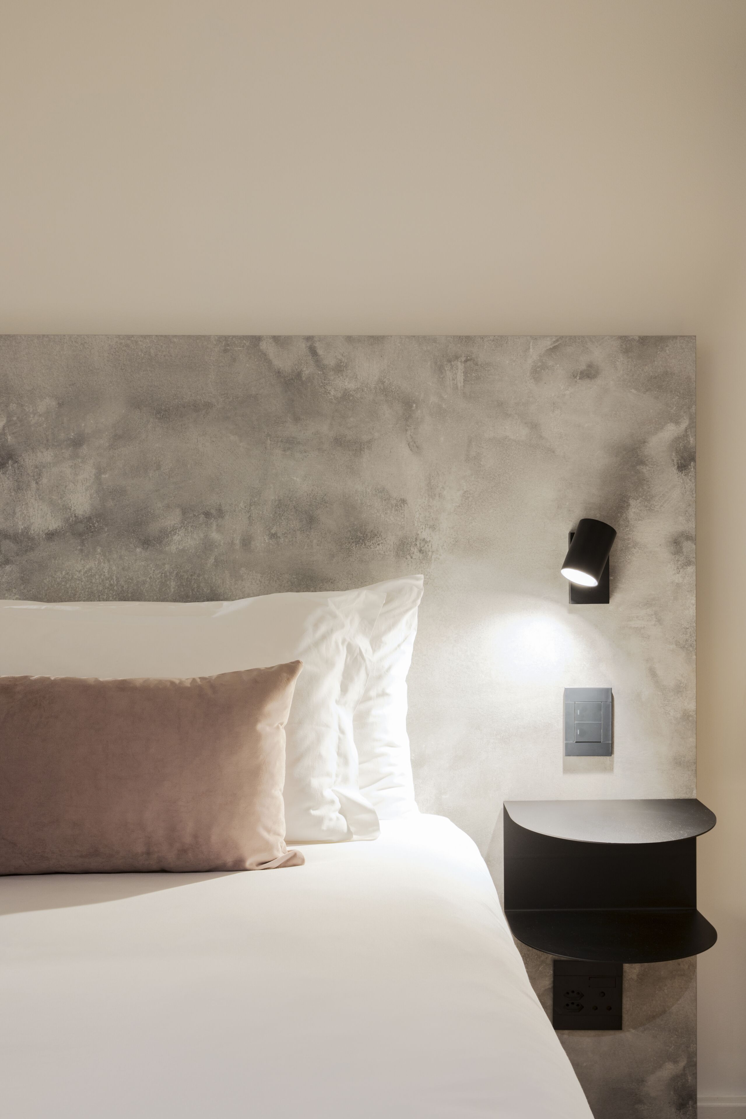 Un dormitorio con una cama, almohadas, una mesita de noche y una lámpara de pared.