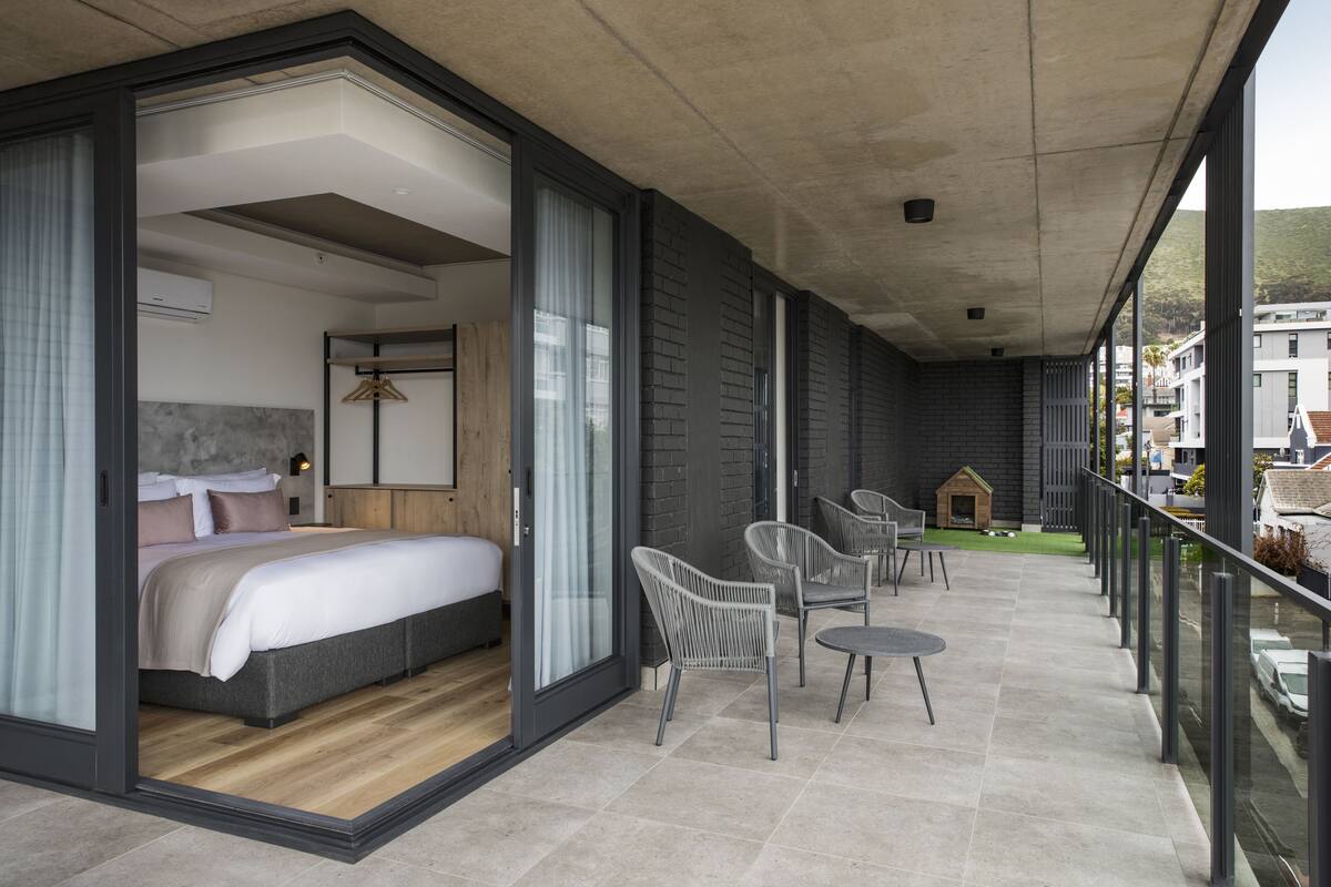 Una habitación de hotel moderna con una cama grande, un balcón con sillas y vistas a la ciudad.