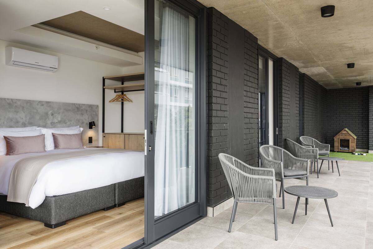 Un dormitorio con cama, puerta corrediza de vidrio que da a un área de estar exterior con sillas y una mesa.