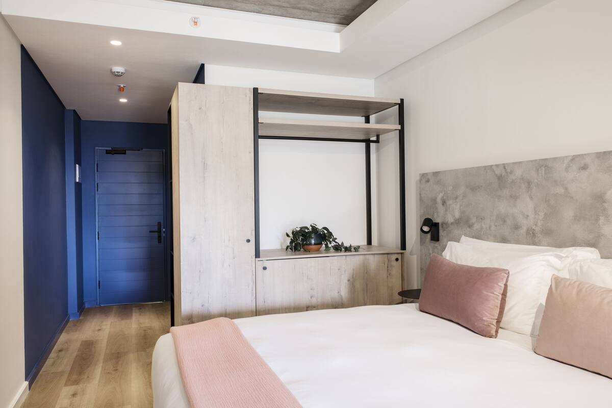 Un dormitorio moderno con cama, armario empotrado, una planta en maceta y vista a una puerta azul.