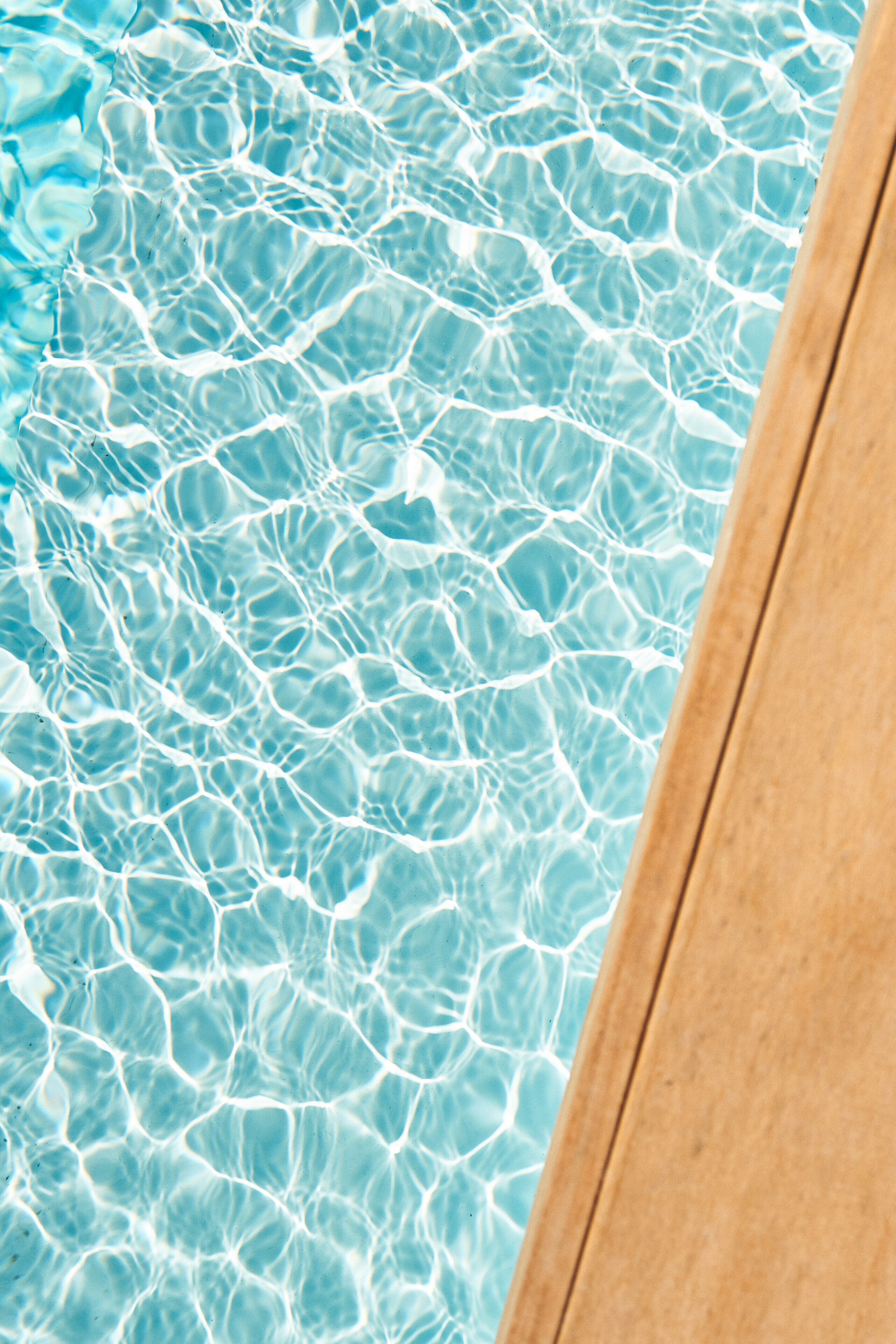 Vista despejada de una piscina con reflejos en el agua y un borde de madera.