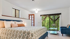 Une chambre avec un grand lit, un bureau et une vue sur une forêt, accessible par une porte coulissante.