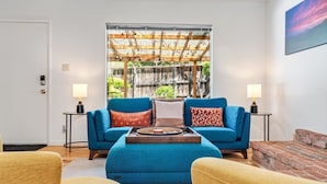 Un salon avec un canapé bleu, deux tables d’appoint avec des lampes, une table basse en bois et une cheminée en briques.