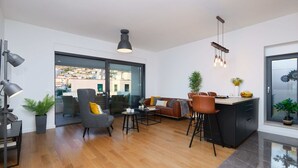 A modern living room with a sofa, armchairs, and a dining area. There is a large window with a view of buildings outside. - Hedera Estate, Hedera A15 (Dubrovnik)