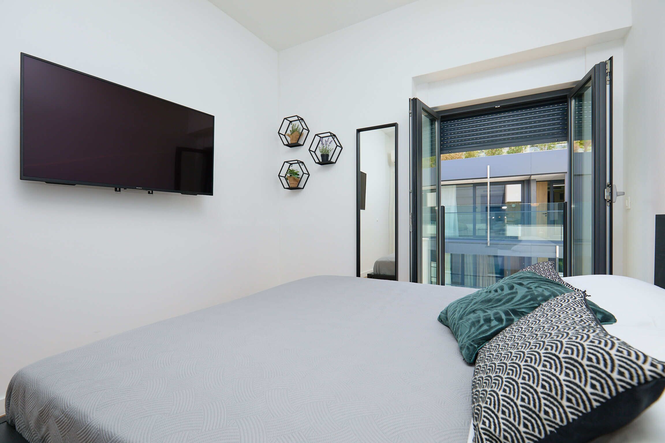 Ein modernes Schlafzimmer mit einem großen Bett, einem flachbildfernseher an der Wand und einem Balkon mit Glastür.
