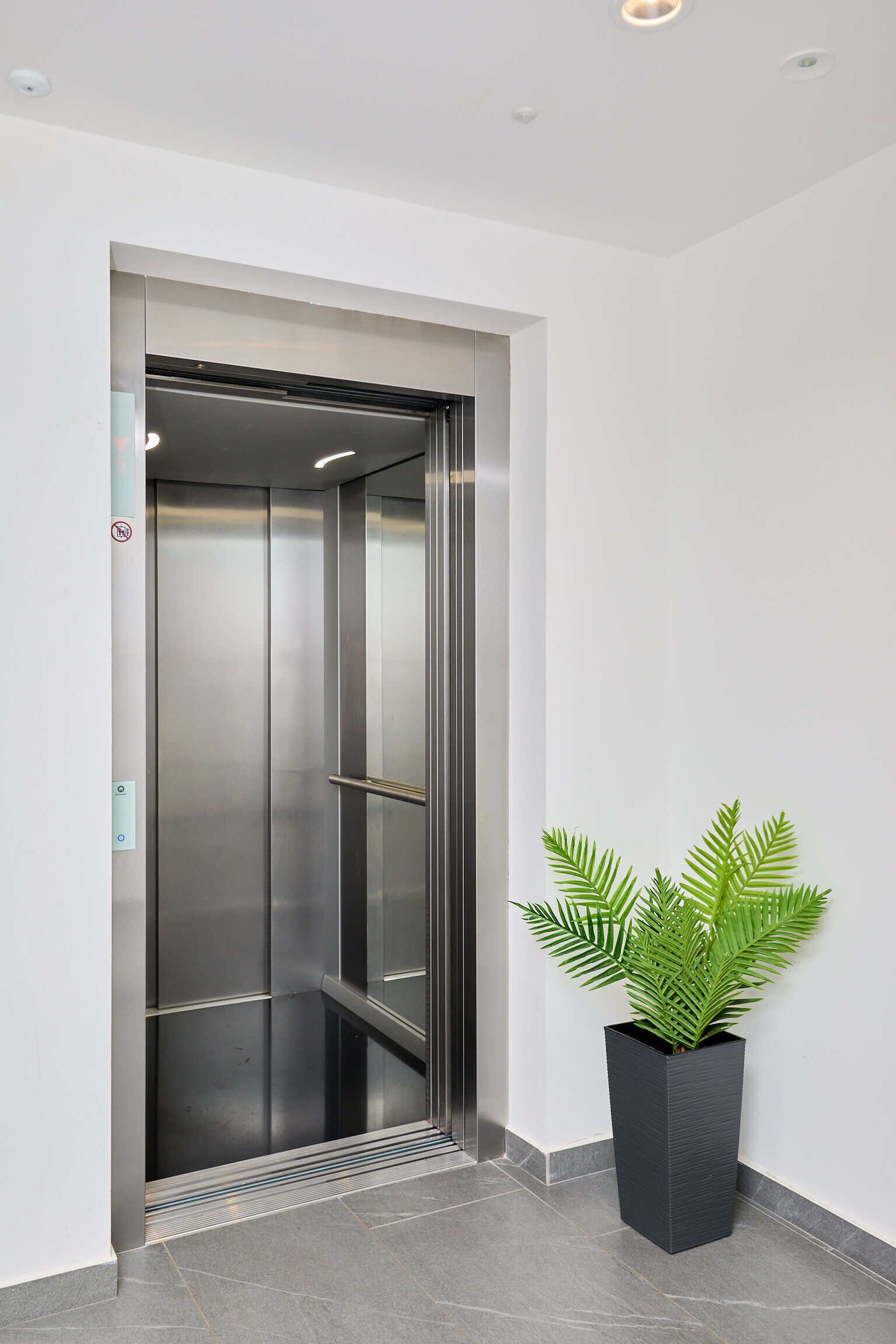 An elevator with a metallic finish, a potted plant beside it, and a tiled floor.