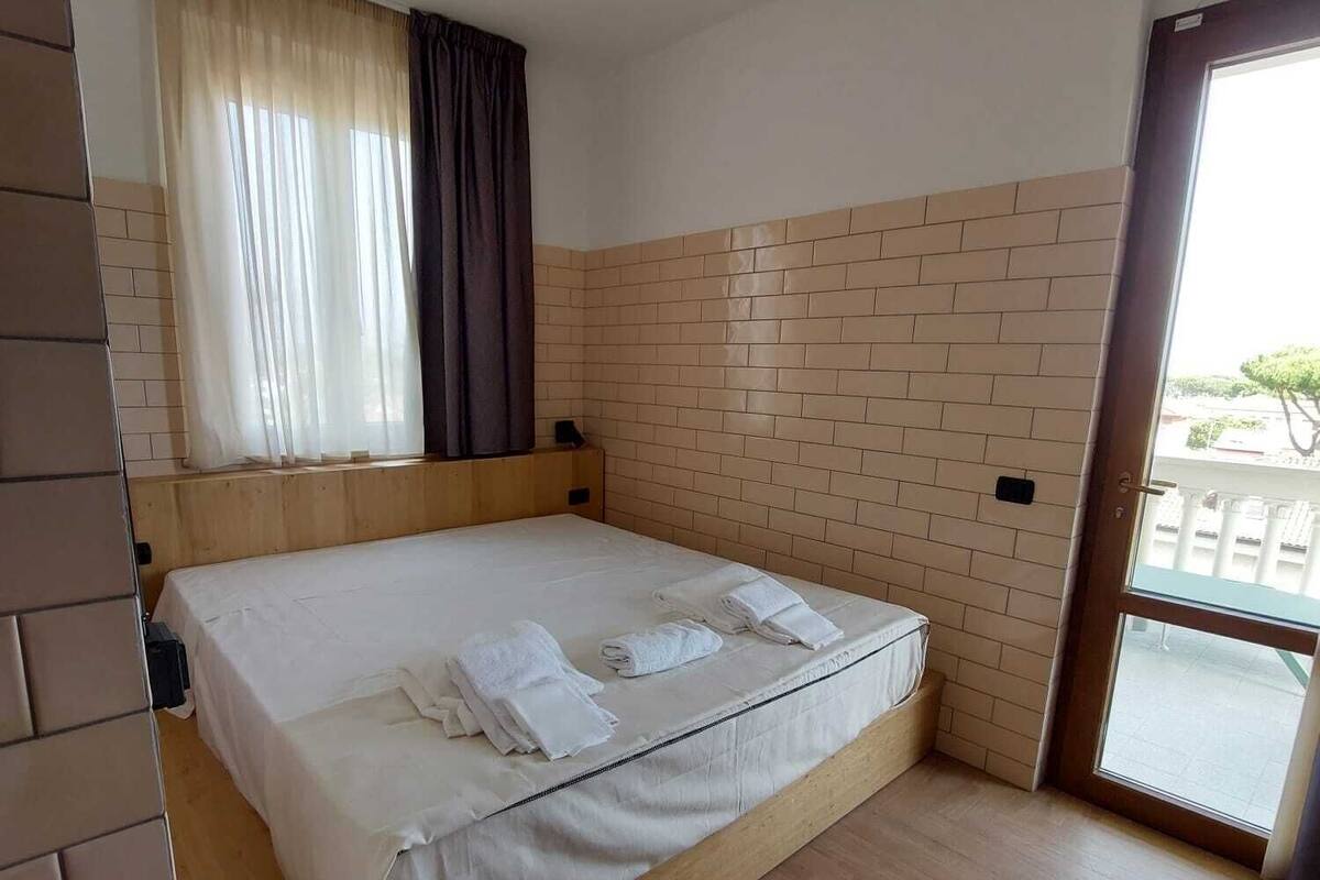 A hotel room with a large bed, a window with curtains, a wooden floor, and a brick-patterned wall.