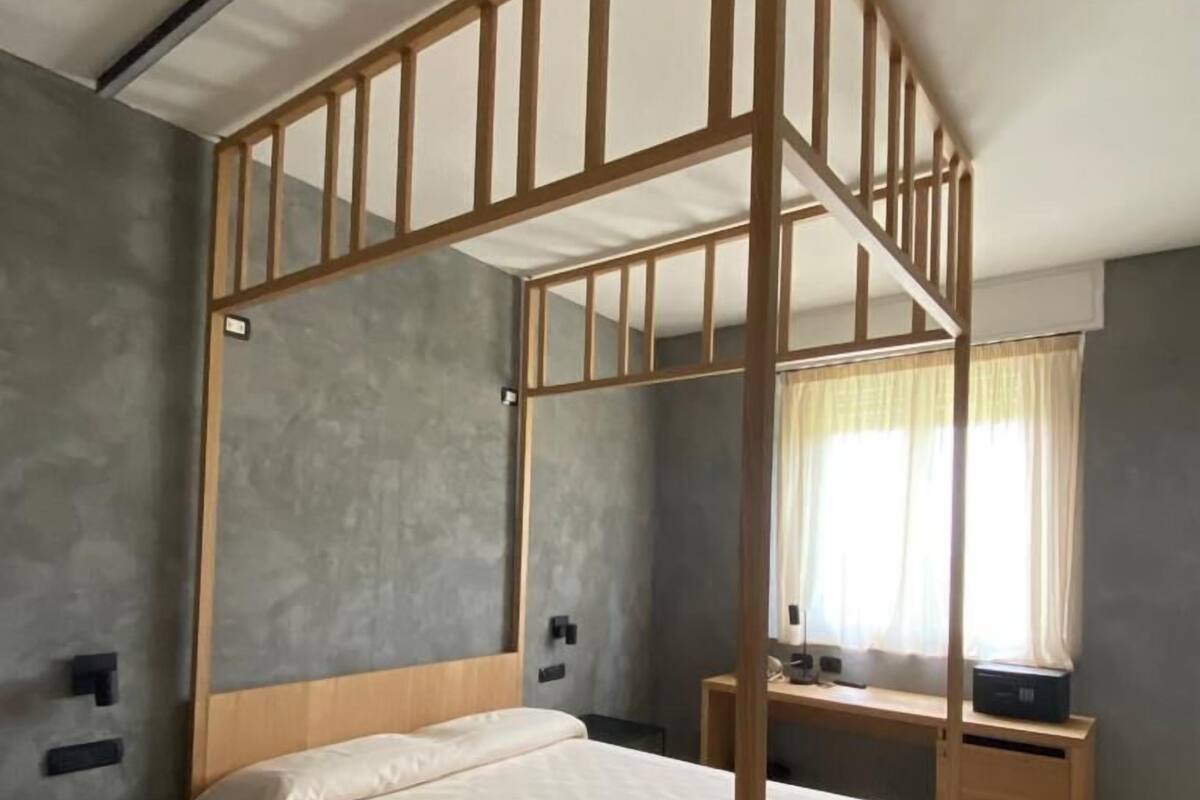 A bedroom with a wooden bunk bed, a bedside table, a desk, and a window with curtains.