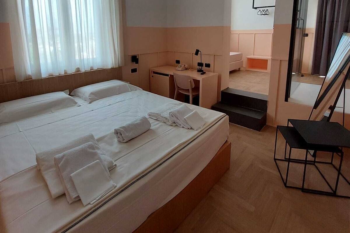 A hotel room with a large bed, a desk, a chair, and a small bathroom.