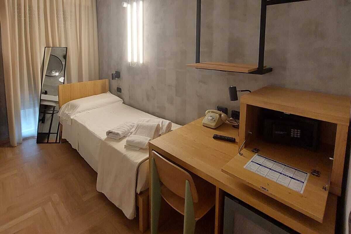 A hotel room with a bed, a desk with a telephone, a chair, a mirror, and a window with curtains.