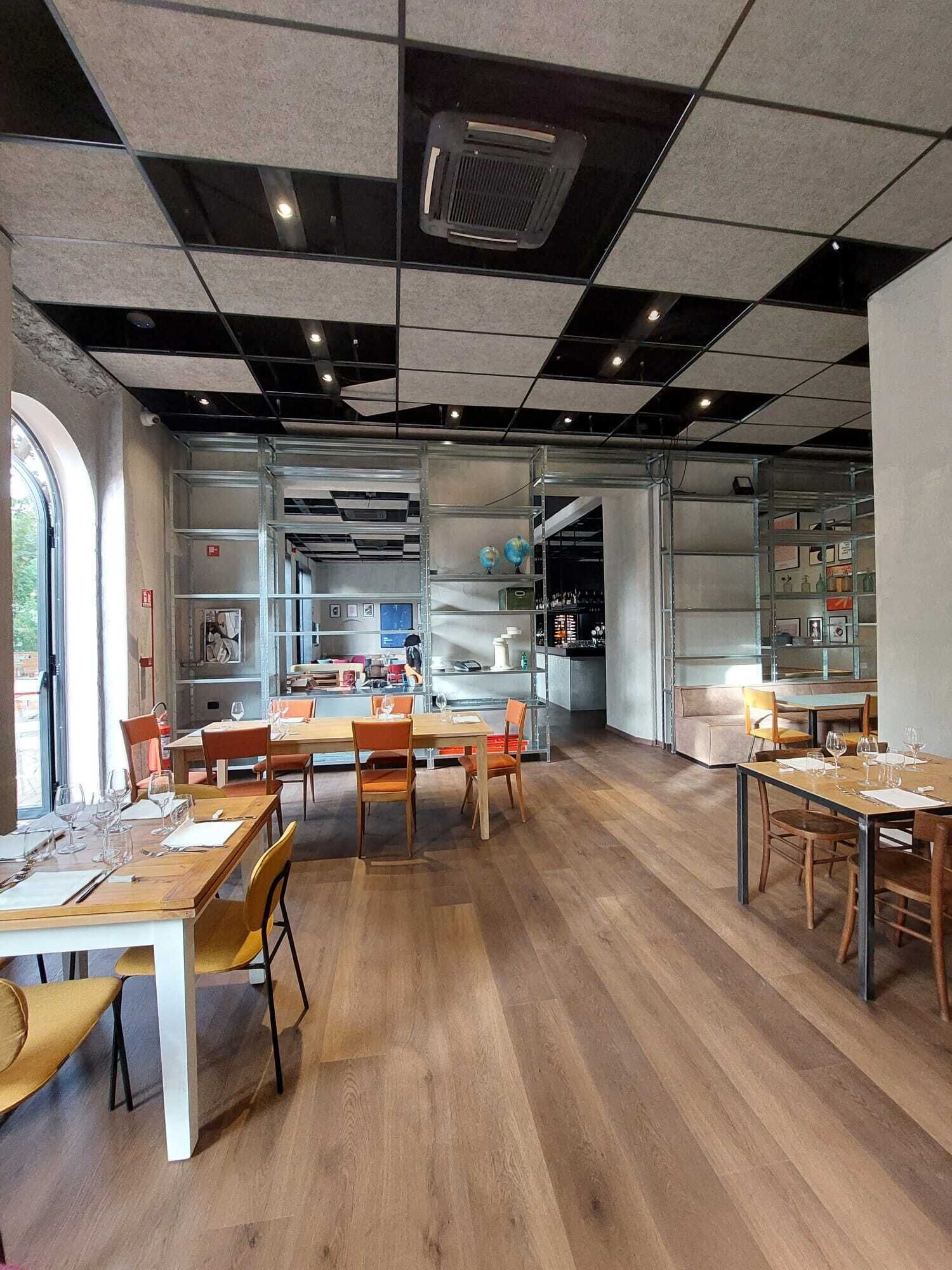Un ristorante moderno con tavoli e sedie in legno, un'area bar e scaffali con diversi oggetti.
