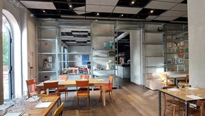 A modern restaurant with wooden tables and chairs, a bar area, and shelves with various items. - RE-Versiliana (Pietrasanta)