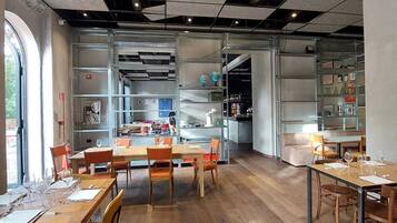 Un ristorante moderno con tavoli e sedie in legno, un'area bar e scaffali con diversi oggetti.