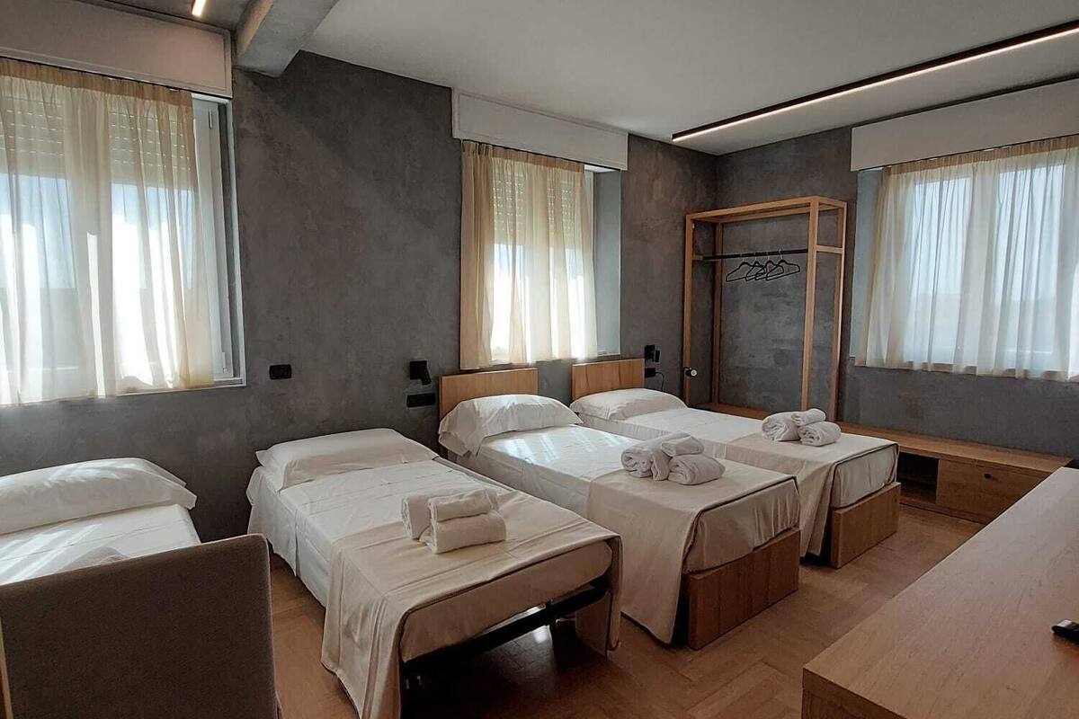 A hotel room with four single beds, a wooden desk, and a mirror.