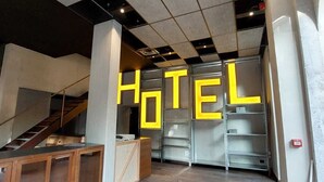 A modern hotel lobby with a staircase, a reception desk, and a large 'HOTEL' sign on the wall. - RE-Versiliana (Pietrasanta)