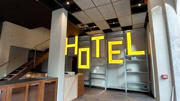 Un'accogliente hall d'albergo moderna con una scala, una reception e un grande cartello con la scritta 'HOTEL' sulla parete.