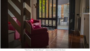 A cozy room with a red sofa, a wooden bench, and a large window with a view of the garden. - The Gulf Sailor's Cottage - Lake Maggiore (Cantone)