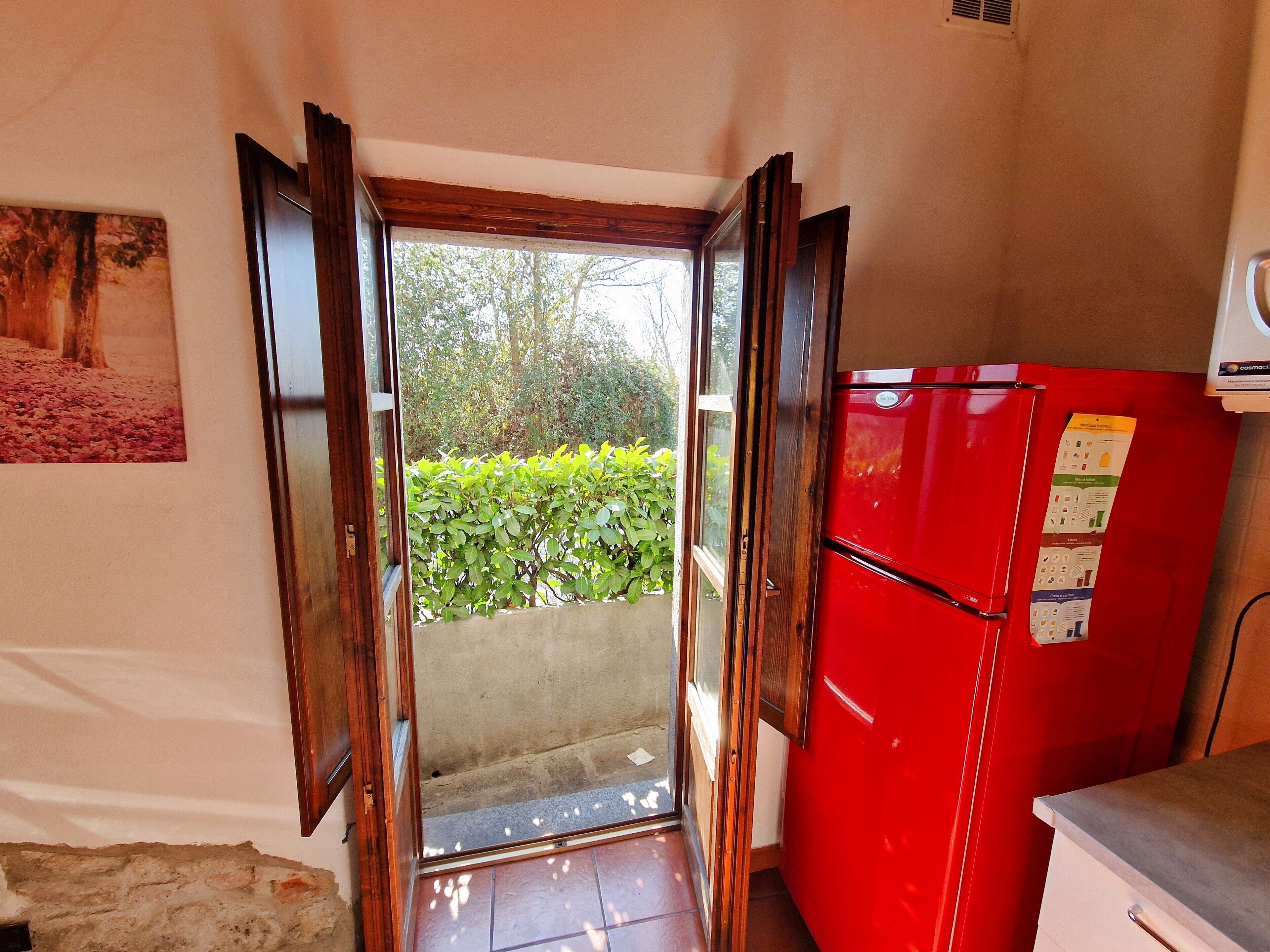 Eine Küche mit einem roten Kühlschrank, einer Holztür, die nach draußen führt, und einem kleinen Fenster.