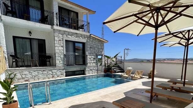 A poolside area with lounge chairs, a pool, and a building with stone facade and balconies. - Serez Otel Alaçatı by La Mira (Cesme)