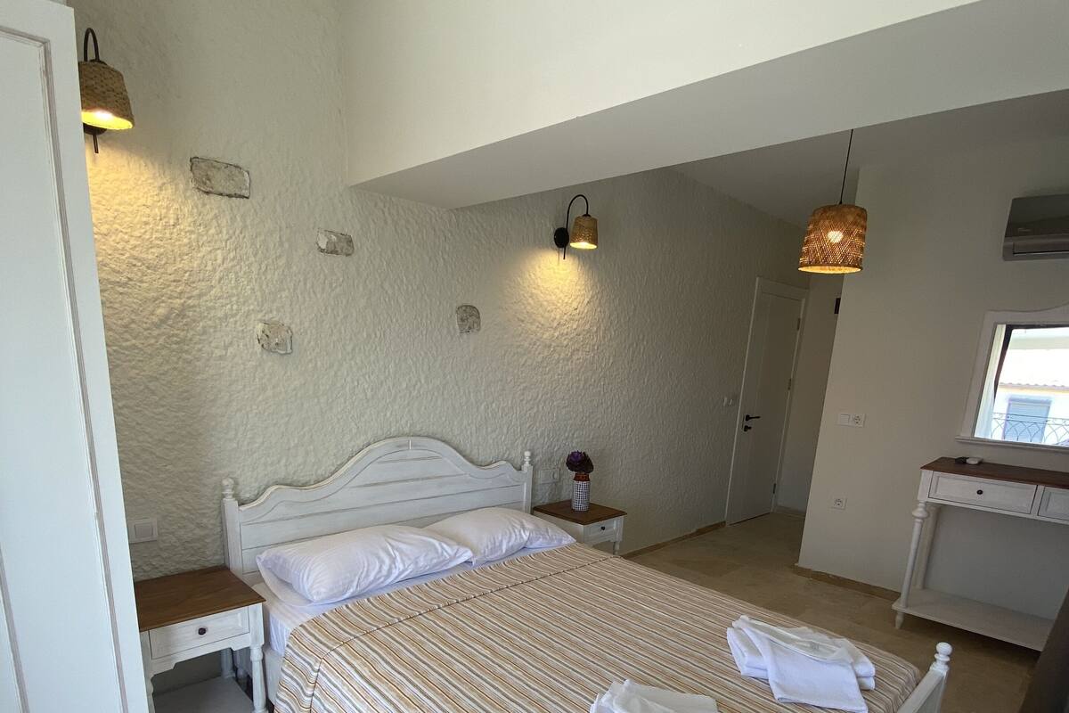 A bedroom with a bed, bedside tables, a desk, and a window.