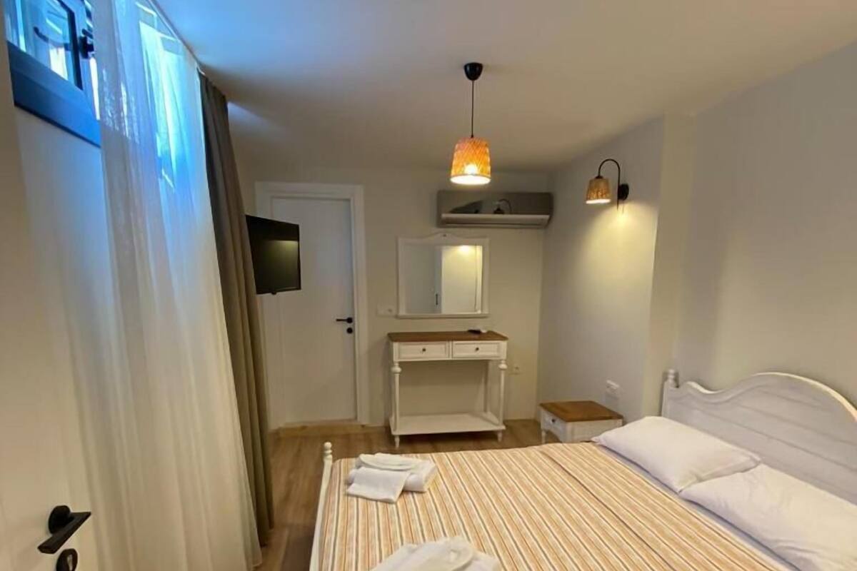A bedroom with a bed, a bedside table, a mirror, a hanging light fixture, and a door.