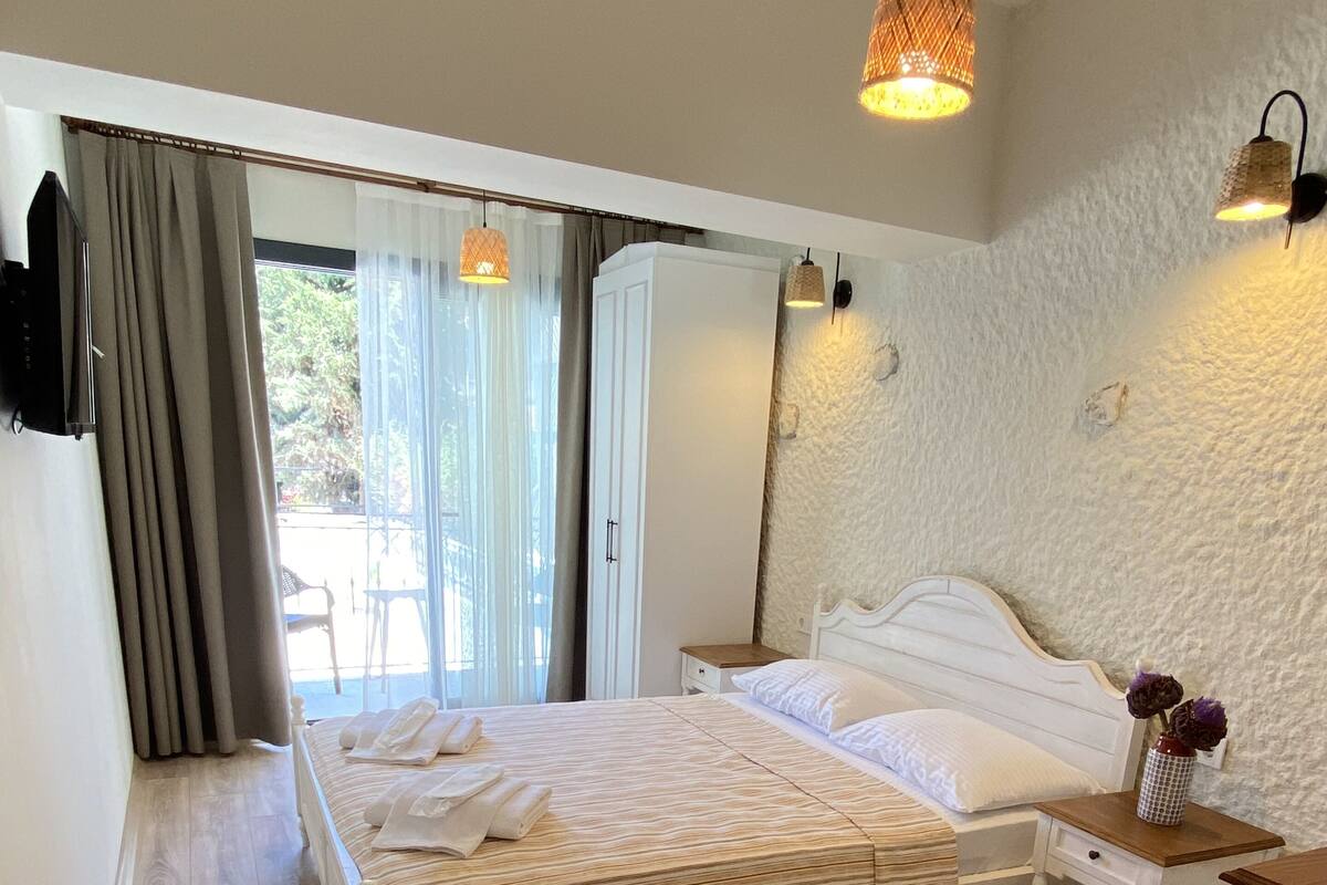 A bedroom with a bed, bedside tables, a wardrobe, and a view of the outdoors.