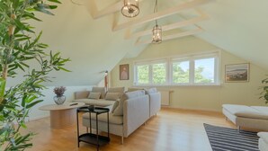 A spacious living room with a high ceiling, wooden beams, a large window, a sofa, a coffee table, and a striped rug. - Large Penthouse Apt - Downtown - Marina (Tórshavn)