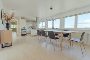 Una cocina moderna con una isla grande, armarios blancos y vistas al exterior a través de amplios ventanales.