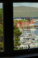 Un puerto deportivo con barcos amarrados, un edificio rojo con techo verde y una colina al fondo.