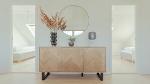 A modern bedroom with a herringbone-patterned dresser, a round mirror, and a vase with dried flowers. - Large Penthouse Apt - Downtown - Marina (Tórshavn)