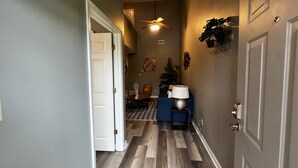 A hallway with a wooden floor, a ceiling fan, a lamp, and a door.