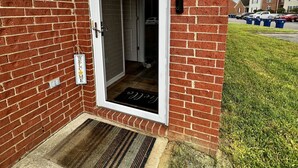 A red brick building with a white door, a welcome mat, and a doormat.