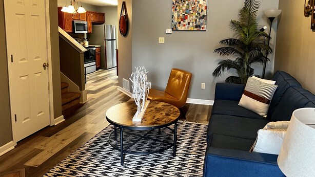 A modern living room with a sofa, coffee table, and a dining area with a chandelier.