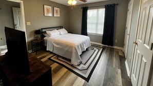 A bedroom with a bed, a ceiling fan, a window with curtains, and a door.
