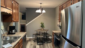 A kitchen with wooden cabinets, a stainless steel refrigerator, a coffee maker, and a dining area with a table and chairs.