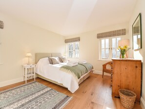 A bedroom with a bed, bedside tables, a dresser, a window with curtains, a patterned rug, and a basket.