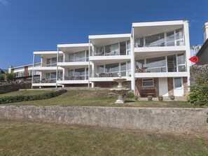 A multi-story building with balconies, a stone retaining wall, and a small fountain.