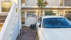 A white car parked in a narrow driveway with a palm tree and a building in the background. - Dual View - 1 Linden Court (Brixham)
