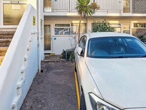A white car parked in a narrow driveway with a palm tree and a building in the background.