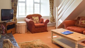 A living room with a television, two armchairs, a coffee table, and a window with curtains. - 2 bedroom accommodation in Lanreath, near Looe (Lanreath, near Looe)