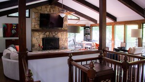 A cozy living area with a stone fireplace, a flat-screen TV, and a wooden balcony railing.