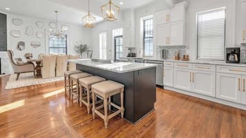 Una cocina moderna con armarios blancos, una isla central, taburetes de madera y luminarias colgantes.
