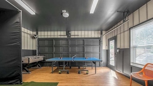 A ping pong table in a room with a wooden floor, a chair, and a window with blinds.