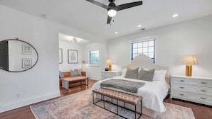 A bedroom with a bed, bedside tables, a bench, a ceiling fan, and a large rug.