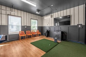 Une pièce aux murs rayés, un espace recouvert de gazon synthétique vert, un téléviseur et un sac de golf.