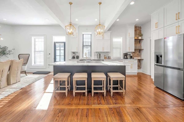 A modern kitchen with a central island, bar stools, pendant lighting, and stainless steel appliances.