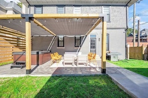 A covered patio with outdoor furniture, a barbecue grill, and a stone pathway leading to a house.